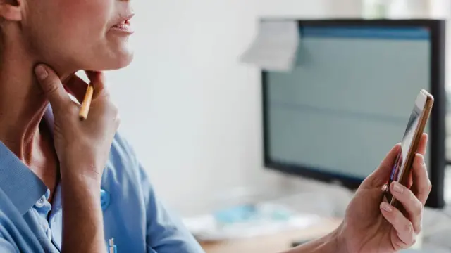 Telefon ekranında boynunu yoxlayan qadının şəkli.