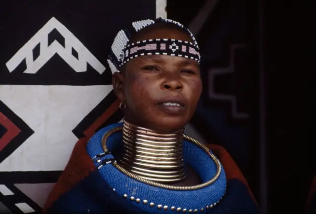 Boynunda çoxsaylı qızıl üzüklər olan orta yaşlı afrikalı qadın.